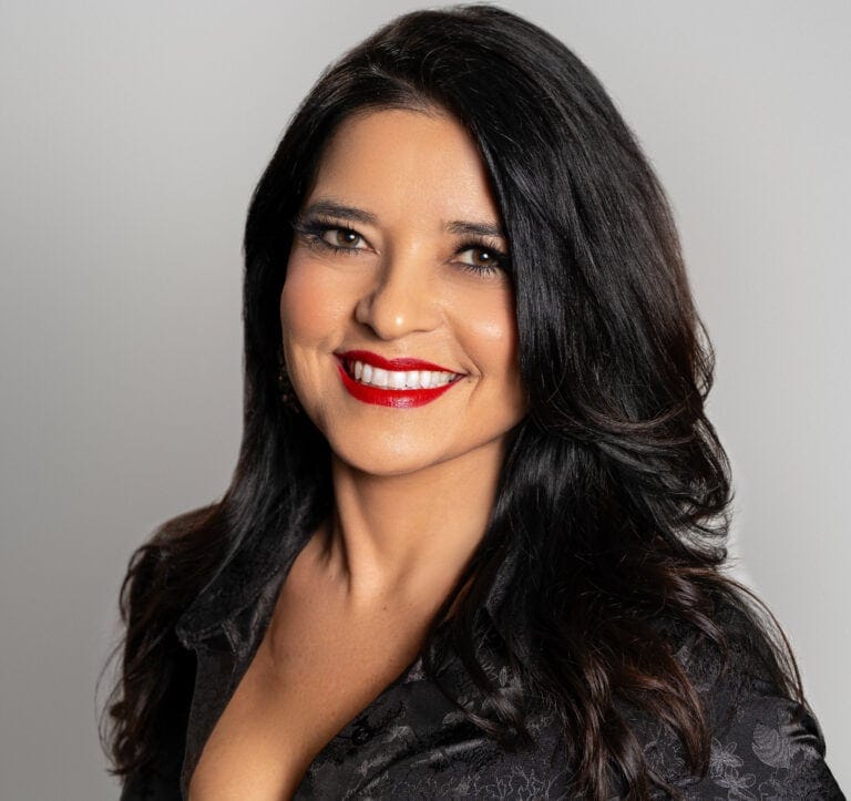 A professional Real Estate Agent, Rhonda Salazar, with long, dark hair and bright red lipstick smiling confidently, dressed in a black patterned top, against a neutral background.