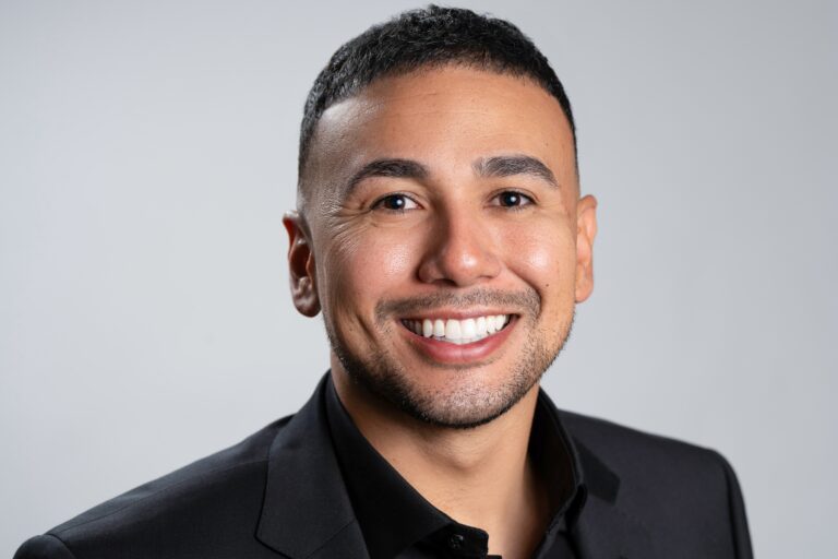 A professional Real Estate Agent, Jeremy Navarro, smiling confidently in a professional black suit, representing leadership and mastery in their field.