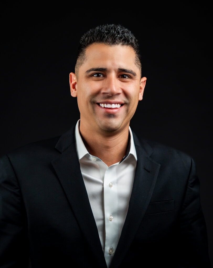 Professional Loan Originator, Julian Cordova, in a black suit smiling confidently against a dark background, representing leadership and success.