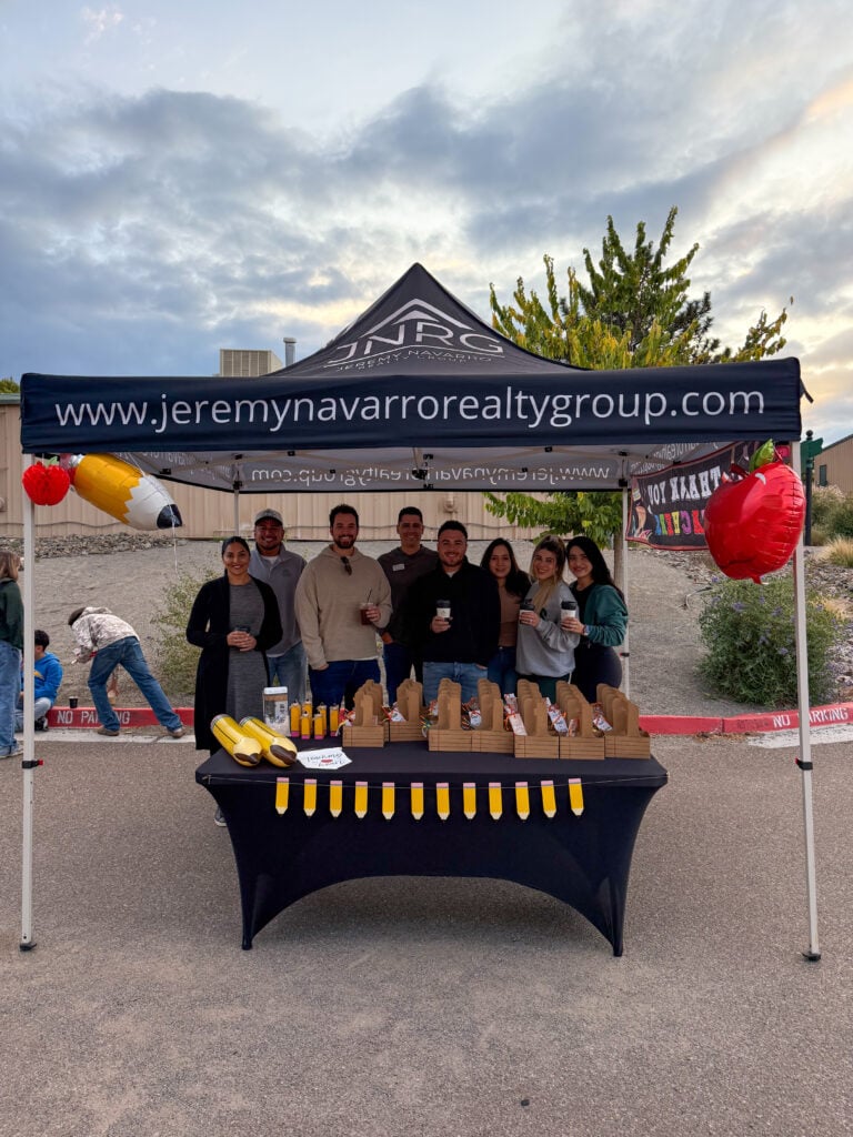Real estate booth at outdoor event with team members and promotional materials, showcasing Jeremy Navarro Realty Group's commitment to client success and community engagement.