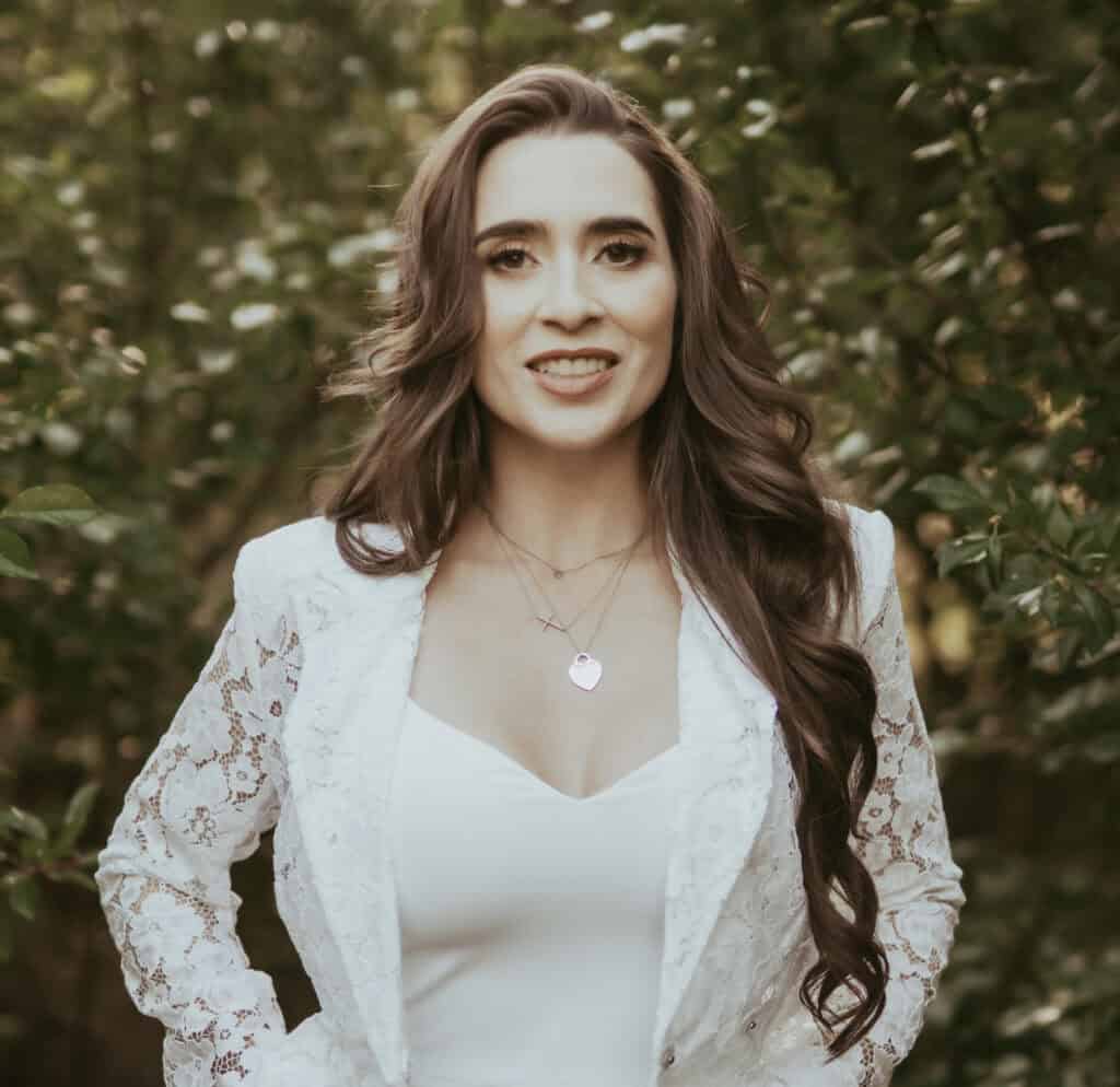 Portrait of Nicole Shepherd, a professional real estate agent in Albuquerque, NM, standing outdoors with greenery in the background.