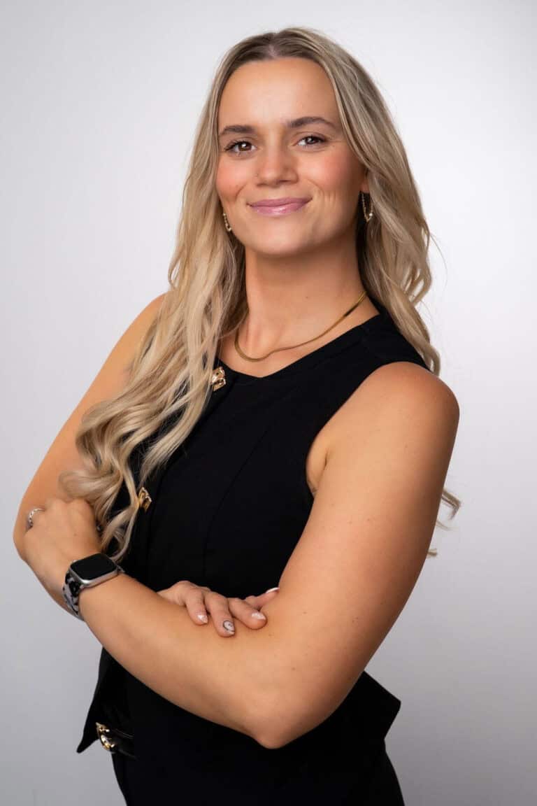 Professional portrait of a confident woman with blonde hair, wearing a black sleeveless top, smiling with arms crossed, in Albuquerque NM.