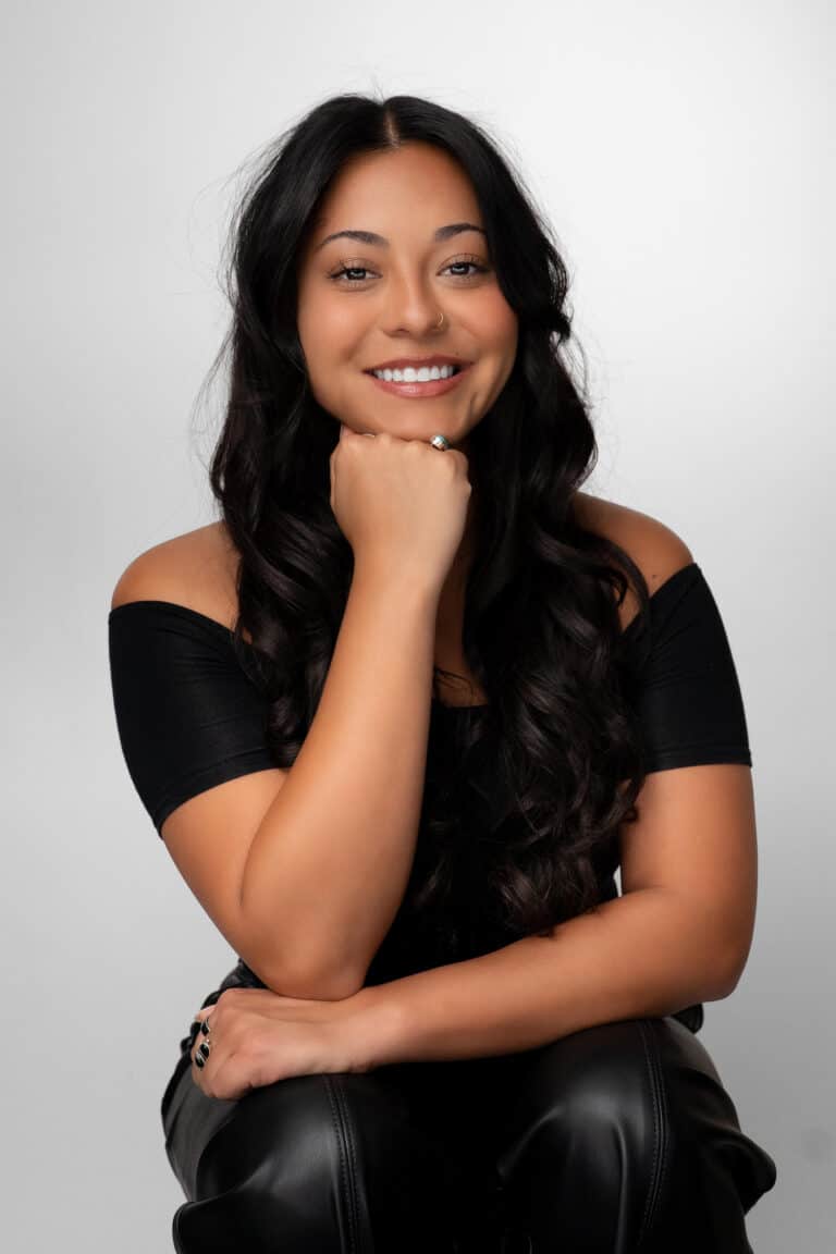 Portrait of Jacqueline Robledo with long dark hair, smiling, wearing a black off-shoulder top, in Albuquerque NM.